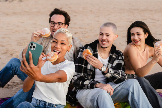 Friends taking selfie while eating donuts at the beach