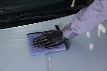 Man polishing car hood with rag indoors, closeup