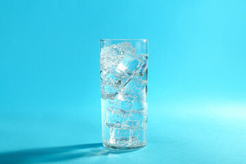 Soda water with ice cubes in glass on light blue background