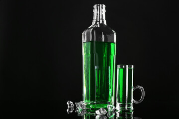 Absinthe in shot glass, bottle and ice cubes on black mirror surface, space for text