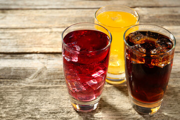 Soda water of different flavors with ice cubes in glasses on wooden table, closeup. Space for text