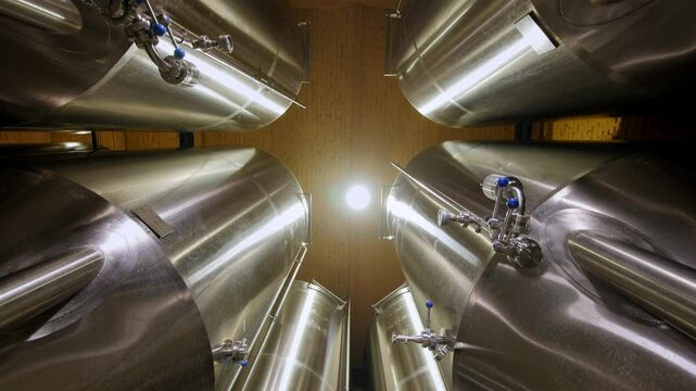 Inside a brewing facility, shiny stainless steel fermentation tanks are arranged symmetrically, creating an industrial ambiance. Stainless steel fermentation tanks. Beer production.