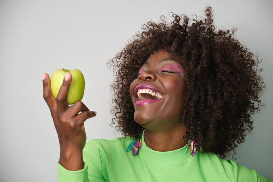 Cheerful african american woman holding a green apple and laughing
