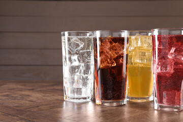 Refreshing soda water of different flavors with ice cubes in glasses on wooden table, space for text