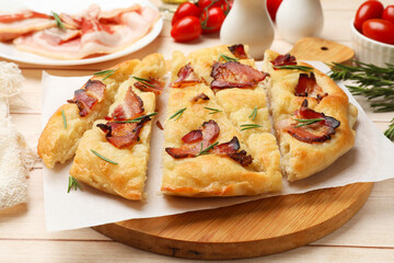 Slices of delicious focaccia bread with bacon and rosemary on wooden table, closeup