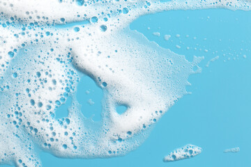 Detergent foam with bubbles on light blue background, top view