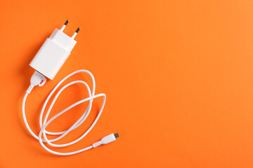 USB power adapter with charge cable on orange background, top view. Space for text