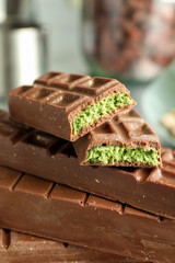 Stack of tasty Dubai chocolate bars with pistachios and knafeh on blurred background, closeup