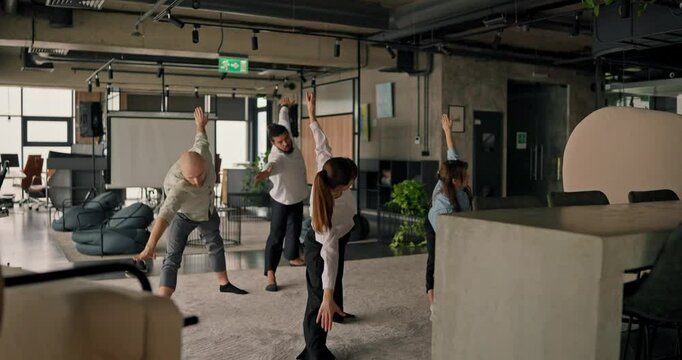A group of office workers stands in a warrior pose practicing yoga and meditation together to support their physical and mental well-being