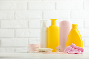 Baby cosmetic products, socks, pacifier and brush on table against white brick wall. Space for text