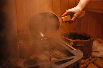 Woman pouring water on stones in sauna, closeup