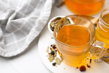 Delicious herbal tea with honey and dry leaves on white table, closeup. Space for text
