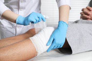Doctor bandaging patient's knee in clinic, closeup