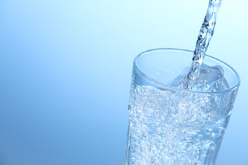 Pouring soda water into glass on light background, closeup. Space for text