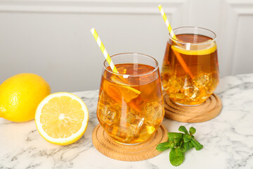Refreshing iced tea with slices of lemon, mint and drinking straws on white marble table, closeup