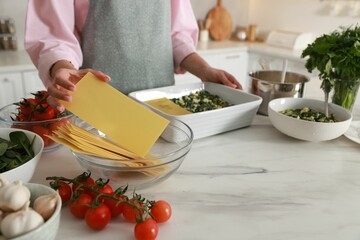 Woman making spinach lasagna at marble table indoors, closeup