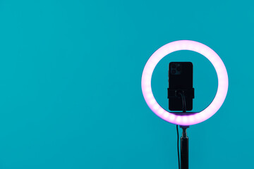 Ring lamp with smartphone on light blue background, space for text