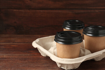 Paper coffee cups in cardboard holder on wooden table, closeup. Space for text