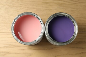 Cans of violet and pink paints on wooden background, flat lay