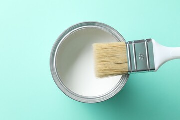 Can of white paint and brush on turquoise background, top view