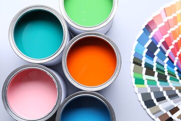 Cans of bright paints and color palettes on light grey background, flat lay