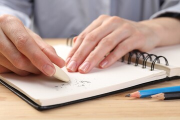 Woman rubbing eraser against paper at wooden table, closeup