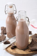 Tasty chocolate milk in glass and pieces of chocolate on white table, closeup