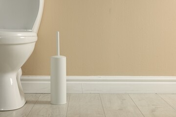 Toilet bowl and brush on floor near beige wall in restroom, space for text