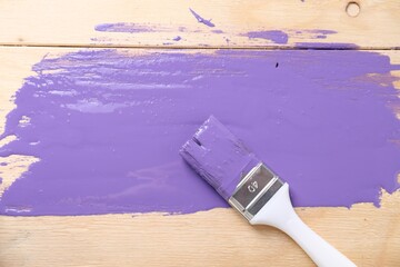 Smear of violet paint and brush on wooden table, top view
