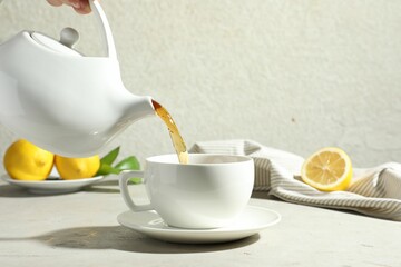 Pouring aromatic tea from teapot into cup at light textured table, closeup