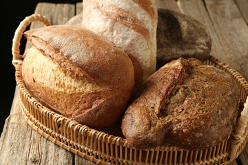 Different loaves of fresh bread in basket on wooden table, closeup
