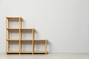 Empty wooden shelving unit near light grey wall indoors. Space for text