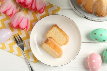 Pieces of delicious bundt cake, Easter eggs and tulips on white wooden table, flat lay
