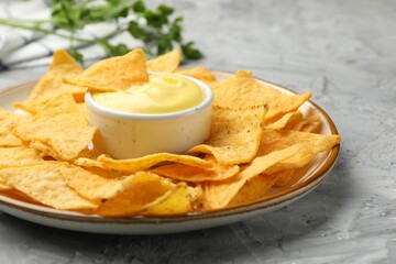 Tasty cheese dipping sauce in bowl, nacho chips and parsley on grey table, closeup