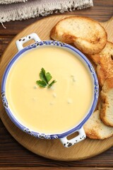 Tasty cheese dipping sauce in bowl and croutons on wooden table, top view