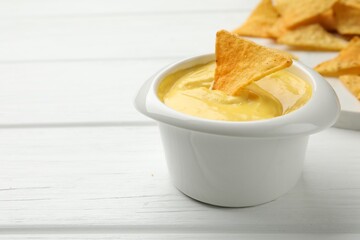 Tasty dipping cheese sauce in bowl and nacho chips on white wooden table, closeup. Space for text