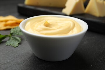 Tasty dipping cheese sauce in bowl, nacho chips and parsley on black table, closeup