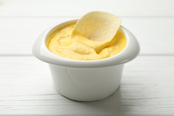 Tasty dipping cheese sauce in bowl and potato chip on white wooden table, closeup