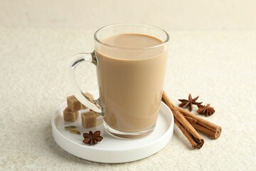 Aromatic Masala tea in glass cup, spices and brown sugar on white textured table, closeup