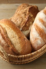 Different types of fresh bread in wicker basket on wooden table, closeup
