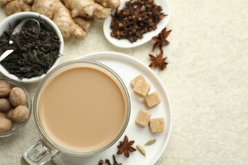 Aromatic Masala tea in cup, spices and brown sugar on white textured table, flat lay. Space for text