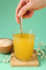 Woman stirring collagen powder in water on turquoise background, closeup