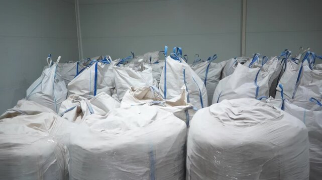 Recyclable materials including polyester and additives stored in massive industrial bags. Sacks with chemicals arranged on floor of manufacturing plant storage area