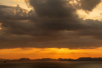 Golden sunset over ocean with mountains, dramatic clouds. Nature
