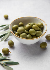 Fresh green olives in a bowl with olive branches on marble table