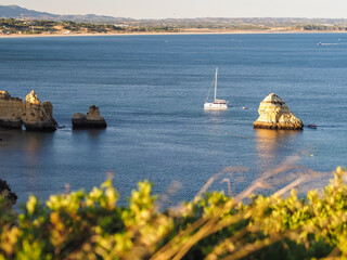 A serene sailboat glides across calm ocean waters near stunning coastal rock formations in Portugal