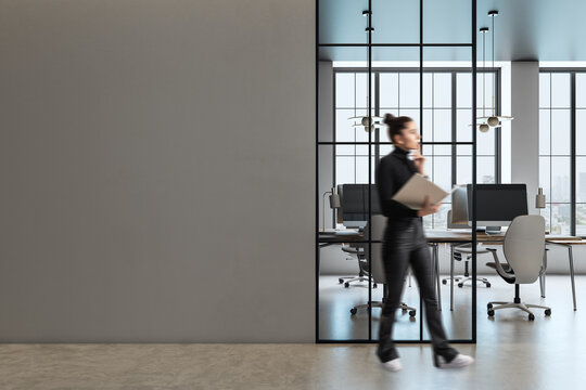 Modern office interior with blank wall and blurred businesswoman.