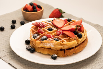 Homemade waffle and mix of raspberries and blueberries as topping. Sweet dessert on white dishes