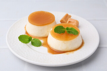 Tasty puddings with caramel sauce served on white tiled table, closeup