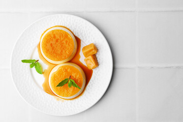 Tasty puddings with caramel sauce served on white tiled table, top view. Space for text